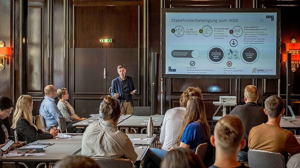 Das Bild zeigt eine Gruppe von Menschen, die in einem Raum an einem Workshop auf der polisMOBILITY teilnehmen und gemeinsam auf einen Redner und großen Bildschirm mit einer Präsentation schauen.