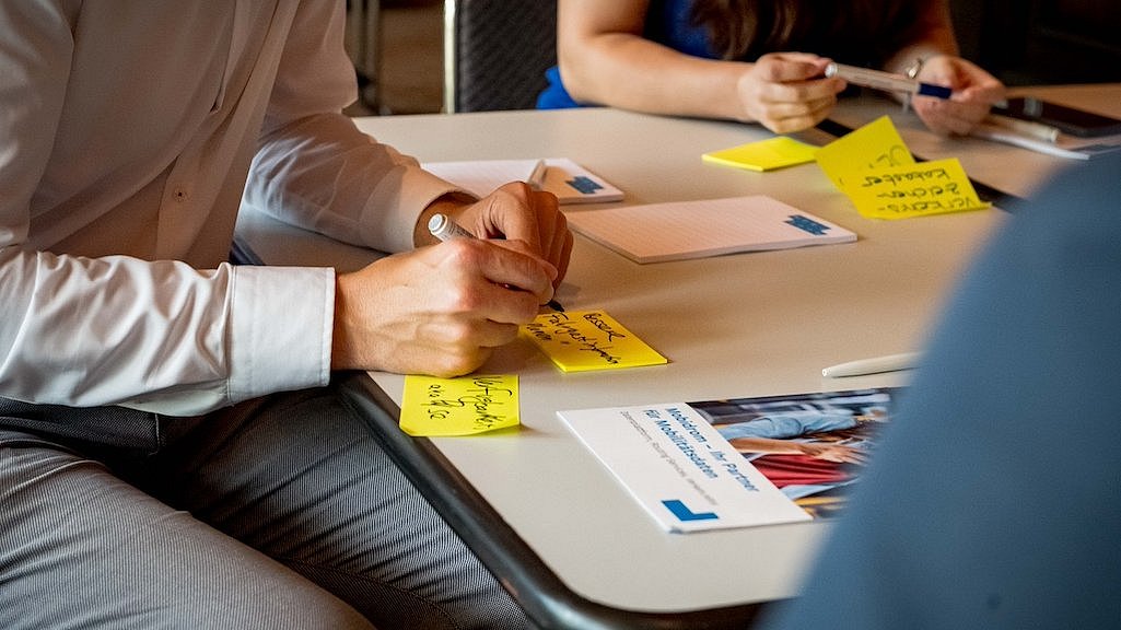 Hände von zwei Personen, die Klebezettel, sogenannte Post-Its, beschriften, auf einem Workshop auf der polisMOBILITY in Köln.