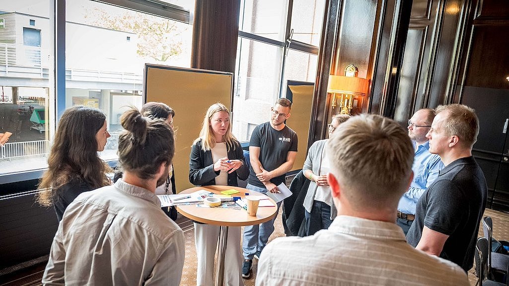 Eine Gruppe von Menschen auf einem Workshop in einem Besprechungsraum mit zwei Pinnwänden vor einer Fensterfront auf der polisMOBILITY in Köln.